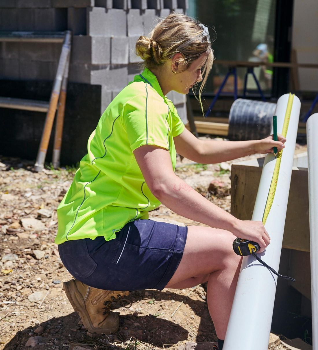 Woman in a Bisley hi-vis shirt measuring pipe on site